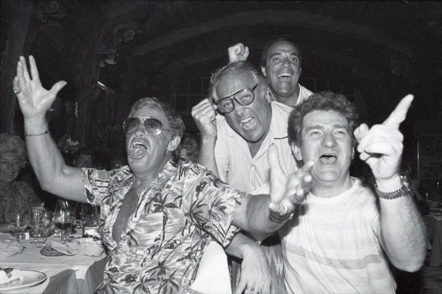 Au restaurant « Les Dents de la mer », Jean-Paul Belmondo, Georges Lautner, Eddy Mitchell manifestent leur joie lors de la finale de la coupe de France de football. Nice, 28 juin 1984. - © Raph Gatti